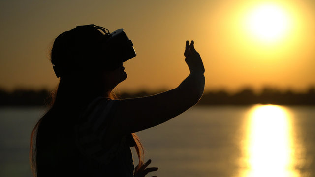 Woman in virtual reality glasses on the sunset background.