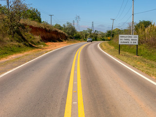 SAO PAULO, BRAZIL - SEPTEMBER 26, 2016 - Road with a new traffic sign informing the new law that requires the use of headlights on even during the day on the roads with a car with lights on