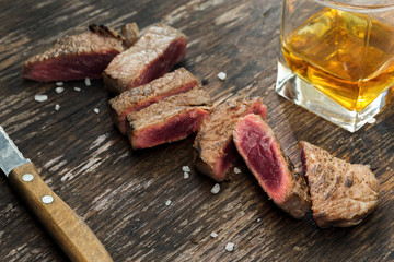 Sliced grilled beef steak on wooden table with whiskey