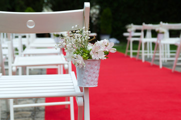 Beautiful detail of wedding decoration, chair for guest decorated with lilies, alstroemerias and chrysanths flowers behind the red carpet. Wedding day concept.