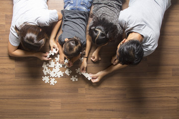 Happy family top view lying on floor with solving a jigsaw puzzle problem and enjoying their...