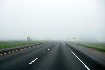 Fototapeta premium Foggy highway with dividing strip marking of green grass and truck with lights on