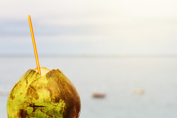 Green coconut with straw facing the sea