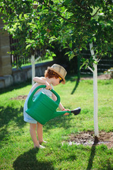little boy watering trees in summer garden