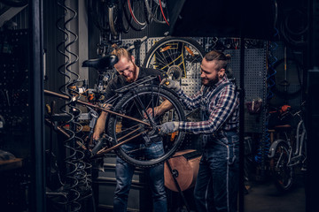 Naklejka na ściany i meble Two bearded mechanics fixing town bicycle in a workshop.
