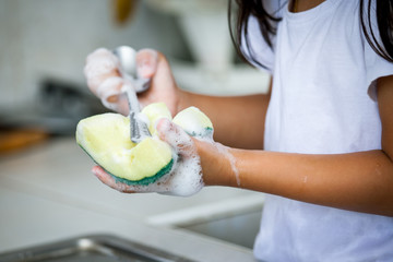 Child hand washing spoon over the sink in the kitchen