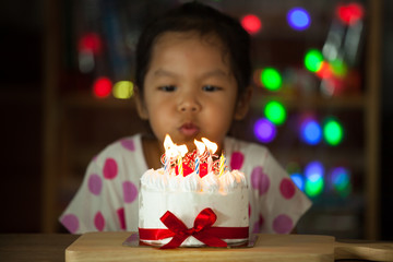 Cute asian little girl celebrating birthday and blowing candles on birthday cake in the party in dark tone