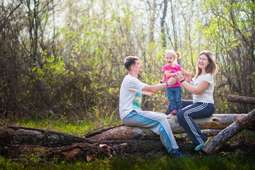Naklejka na ściany i meble Family is resting in nature. Father throws her daughter up. Mom catches up with her daughter. Happy family on vacation at a picnic. Family photo in spring, summer