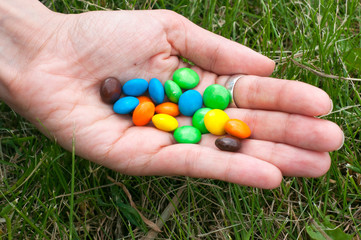 Colorful chocolate candies on hand of pretty girl isolated on grass background
