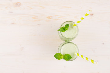 Freshly blended green apple fruit smoothie in glass jars with straw, mint leaf, top view. White wooden board background, copy space.