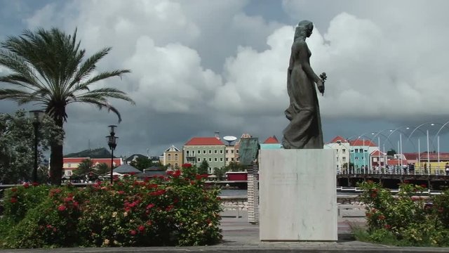 Pan across the waterfront of Willemstad, Curacao past a statue to the Queen Emma Bridge