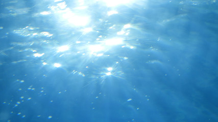 Beautiful underwater sea scene view with natural light rays, shining through the water's glittering, moving surface and blurred bokeh