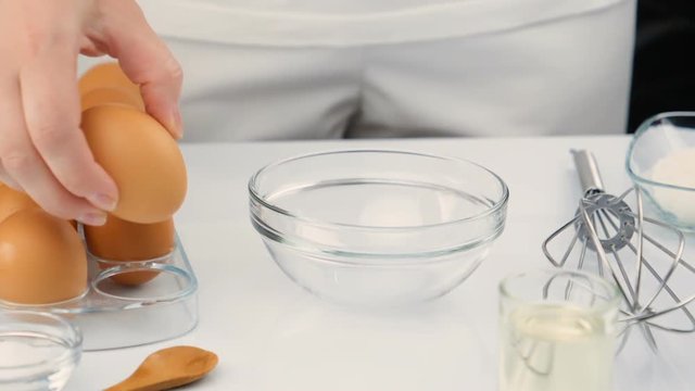 Breaking eggs in a glass bowl. Fresh organic eggs falling into bowl. Preparing ingredients for baking. Slow motion footage at 180fps.