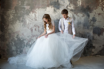 Fototapeta na wymiar The groom straightens the bride's dress against the gray wall. Loft style.