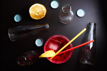 Negroni red cocktail with a slice of lemon with two tubes of red and yellow on a black background, around the empty bottles and caps. Top view/view from above