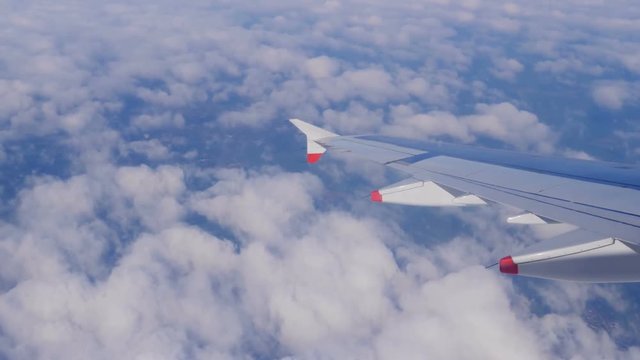 Wing of an airplane flying above the clouds, shot from the window of the plane. Airplane flying above earth at 10000 m -50 °C  (-58.0 °F). Ice and dust on airplane window. 4K footage at 60fps.