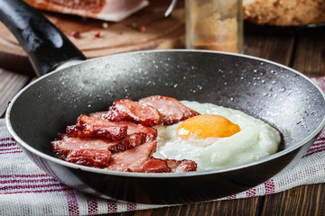 Slices of smoked bacon and fried egg in frying pan