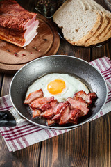 Slices of smoked bacon and fried egg in frying pan
