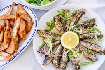 Freshly grilled sardines on a plate with lemon and fried potatoes