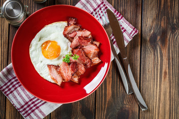 Slices of smoked bacon and fried egg on a red plate