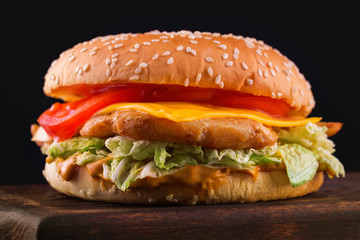Closeup image of tasty cheeseburger on wooden board at dark background.