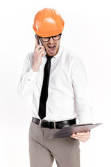 Young construction engineer in orange helmet with folder talking on phone on white background