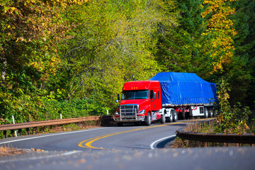 Fototapeta na wymiar Red semi truck flat bed trailer on winding autumn highway