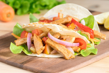 Grilled meat with onion and bell peppers, tomato,lettuce and serve with flour tortilla on wooden board.