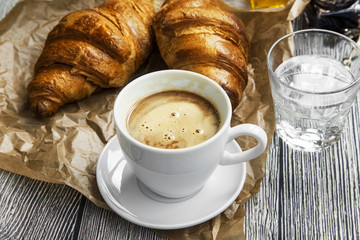 Coffee cup with croissants buns and water glass, morning breakfast meal or coffee