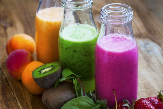 Fresh healthy three types of fruits juices or smoothies bottles, orange, green and pink with strawberries, apricots and kiwi