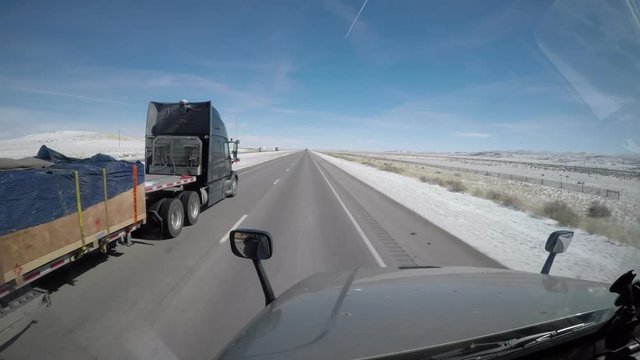 A Flatbed Semi Truck Passes the viewer on a rural highway in Wyoming, USA.