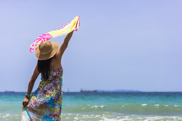 Young woman in summer dress standing on sand and holding straw hat looking to a sky