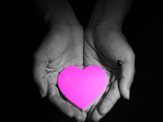 Pink heart in woman hands, low key picture style, dark and black background. love concept.