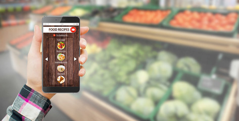 Hand holding smartphone with food blog interface with vegetables in background
