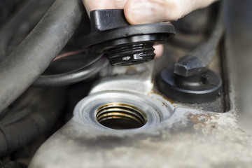 Ręce mechanika samochodowego odkręcają korek wlewu oleju. Mechanik w rękawiczkach jednorazowych odkręcił korek wlewu oleju w silniku. Korek wlewu oleju odkręcony. Ręka trzyma korek.