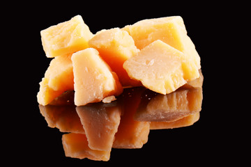 Parmesan cheese on a black glossy table with reflection. Parmesan cheese isolated on black background.