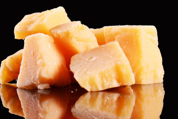 Parmesan cheese on a black glossy table with reflection. Parmesan cheese isolated on black background.