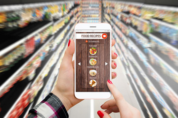 Woman in supermarket using smartphone for food recepies
