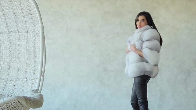Young stylish brunette girl demonstrates fashionable arctic fox fur short coat in studio