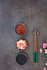 Sushi Set. Japanese sushi chopsticks,  soy and chili sauce bowl and pickled ginger on dark stone background
