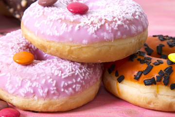 Assortment of colorful donuts with candies on pink wooden background