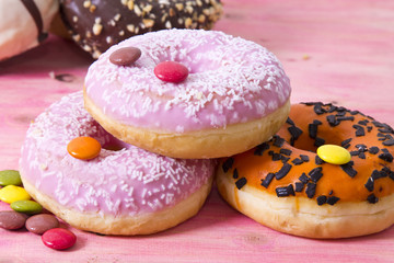 Assortment of colorful donuts with candies on pink wooden background