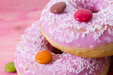 Assortment of colorful donuts with candies on pink wooden background