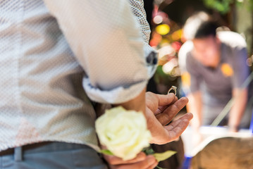 Focus the the Man hold the ring, Men hide the ring and white rose behind with surprise.