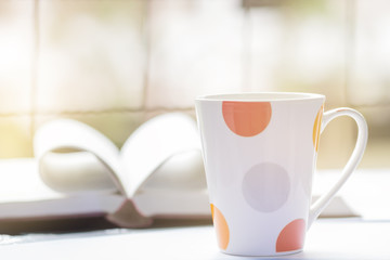 White and red cup coffee against book blur background window on table, pastel tone