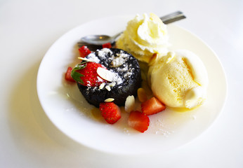 Black chocolate cake with red strawberry and vanilla ice cream on the white dish and cutlery - Dessert concept