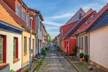 View down a historic cobble stone street with old colorful fishing cottages on a sunny day.