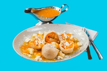 Apricot dumpling, sauce in vessel. On blue background, closeup.