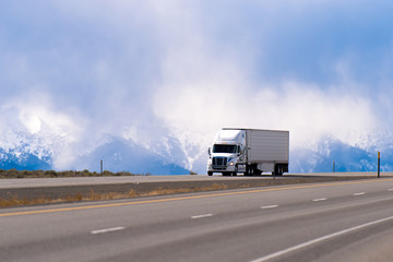 Spectacular white semi truck trailer reefer on highway in snow mountains sky clouds