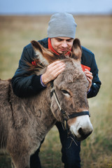 Der lustige Mann umarmt den Esel freundlich. Ein komisches Foto. Schäfer. Herbstfeld.